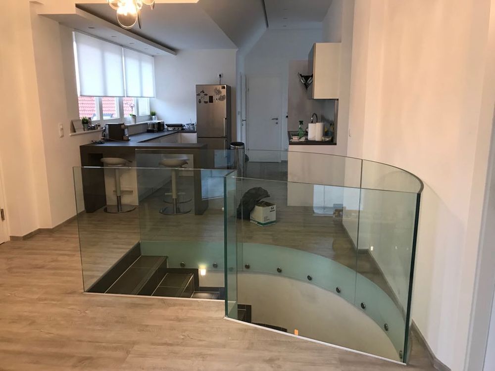 Gebogene Glasbrüstung um eine Treppenöffnung in einem Wohnraum