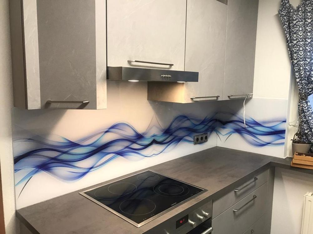 Küchenrückwand aus Glas mit blauem Wellenmotiv, fugenlos über Kochfeld und Arbeitsplatte geführt